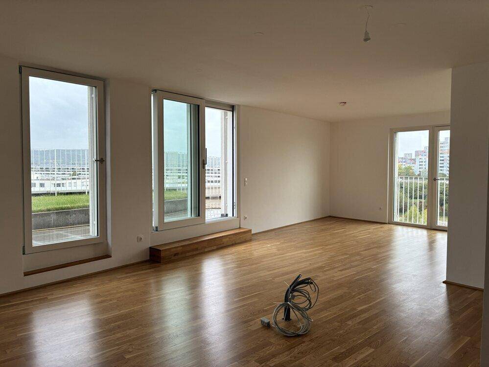 Lichtdurchflutetes Wohnzimmer mit Parkettboden, weißen Wänden und Zugang zu Terrasse und französischen Balkonen.