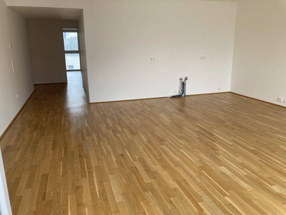 Geräumiger, leerer Wohnbereich mit Parkettboden und vorbereiteten Anschlüssen für eine offene Küche.