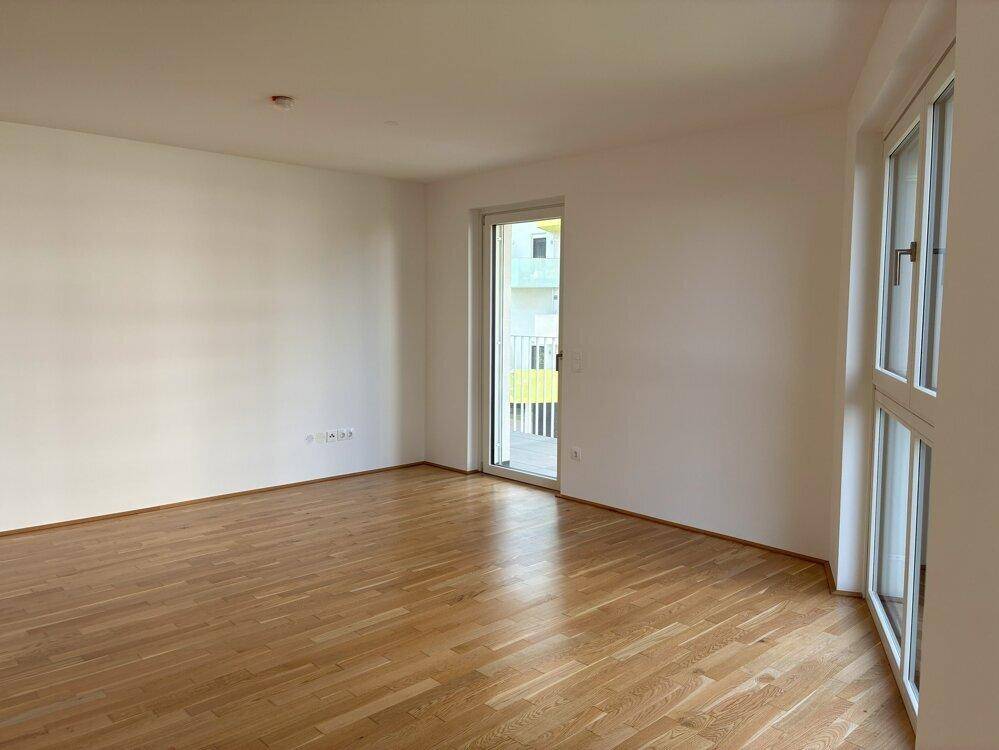 Heller Raum mit Parkettboden und Zugang zu einem Balkon, ideal als Wohn- oder Schlafzimmer.