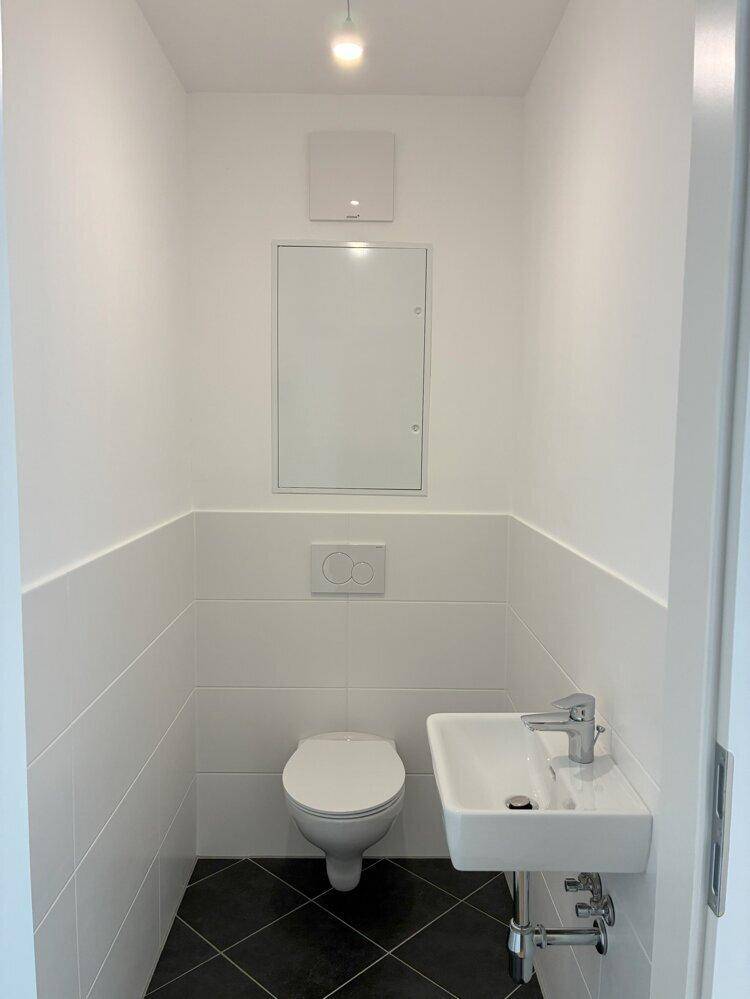 Modernes Gäste-WC mit Wand-WC, kleinem Waschbecken und dunklen Bodenfliesen, minimalistisch gestaltet.