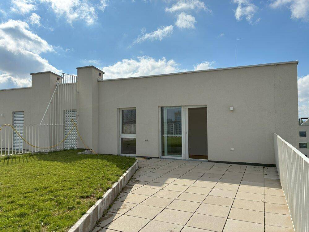 Weitläufige Dachterrasse mit Rasenfläche und gepflastertem Bereich unter blauem Himmel.