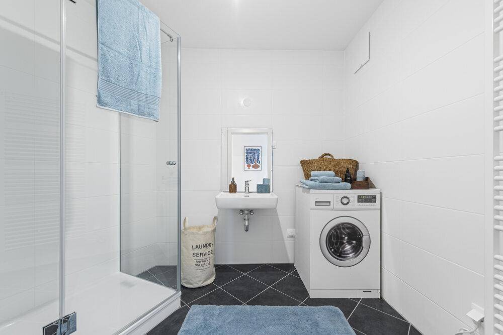 Modernes Badezimmer mit Duschkabine, Waschbecken und integrierter Waschmaschine.
