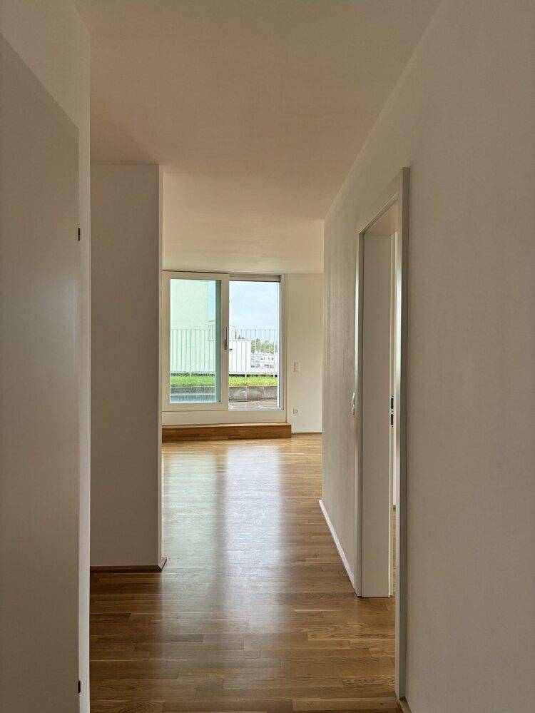Heller Flur mit Parkettboden und Zugang zu einem Wohnbereich mit großen Fenstern und Ausblick.
