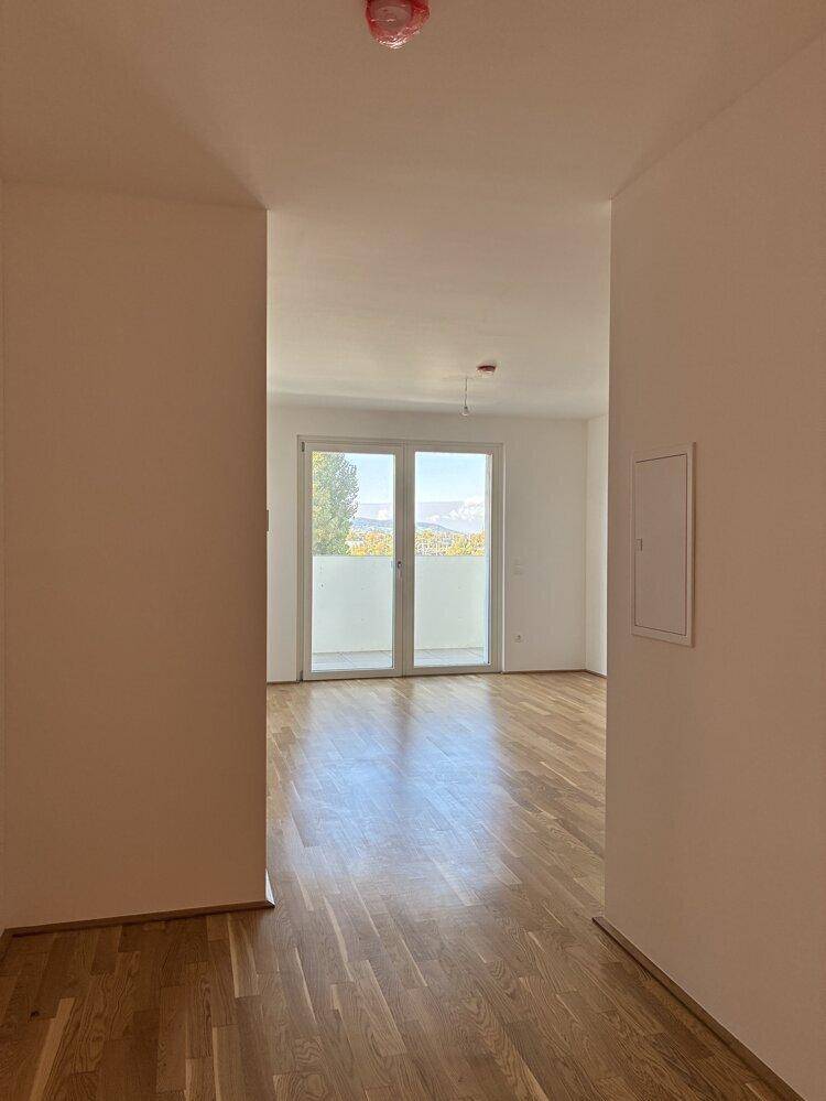 Heller Flur führt zu einem Zimmer mit Balkonzugang und Fernblick auf die Berge.