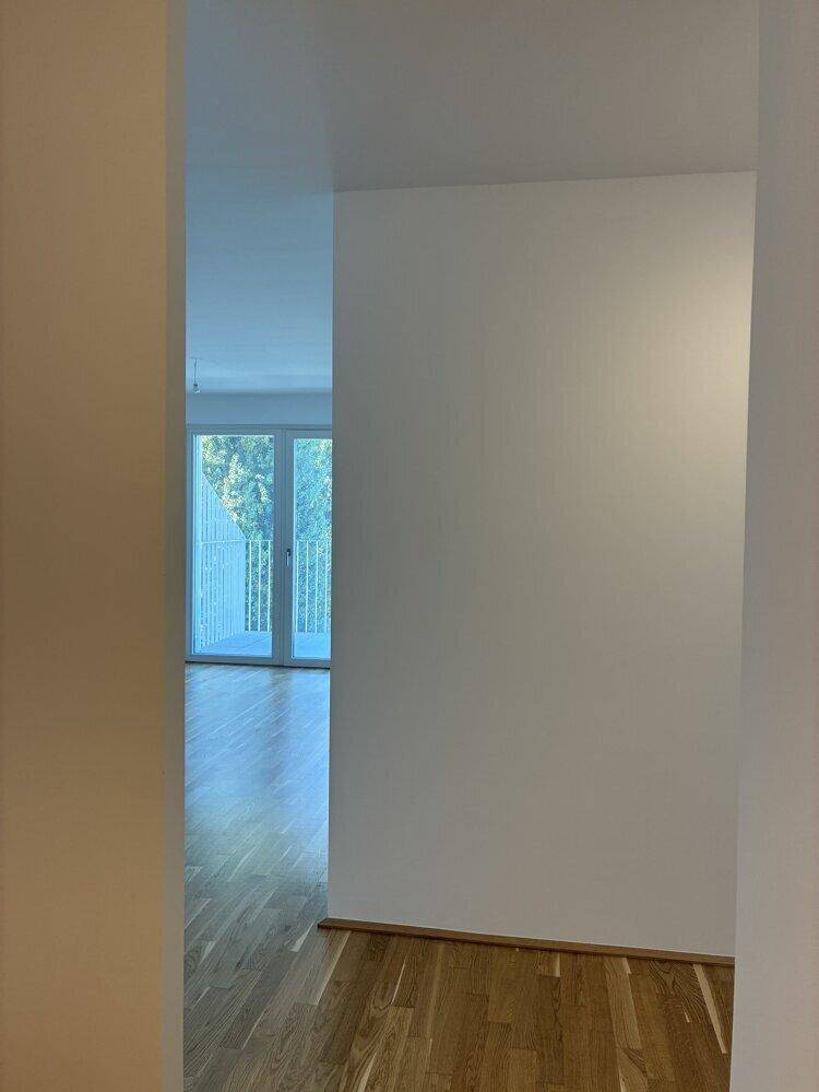 Heller Flur mit Parkettboden, der zu einem Zimmer mit Balkonzugang führt.