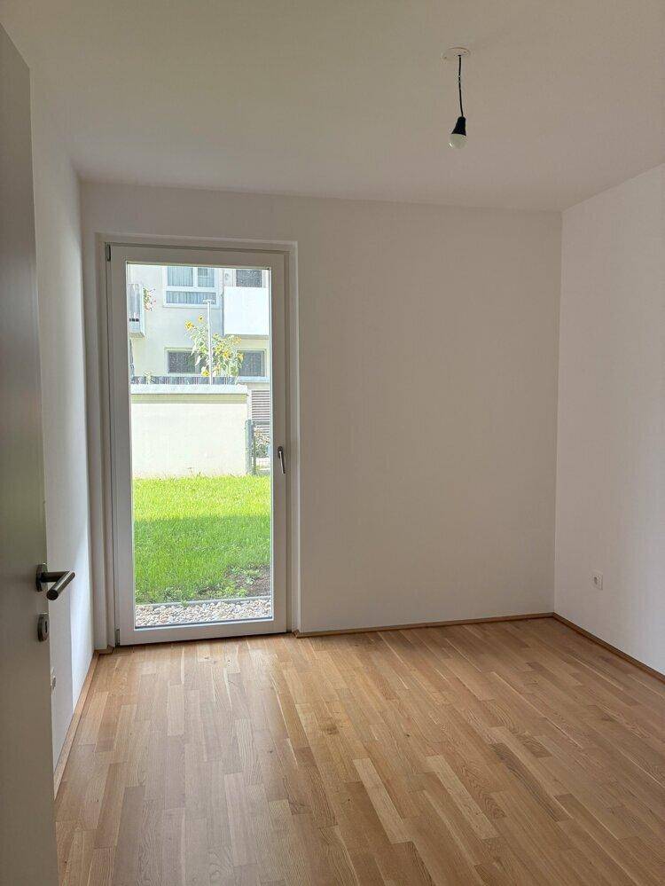 Leeres Schlafzimmer mit Holzboden und direktem Zugang zum Gartenbereich durch eine Glastür.