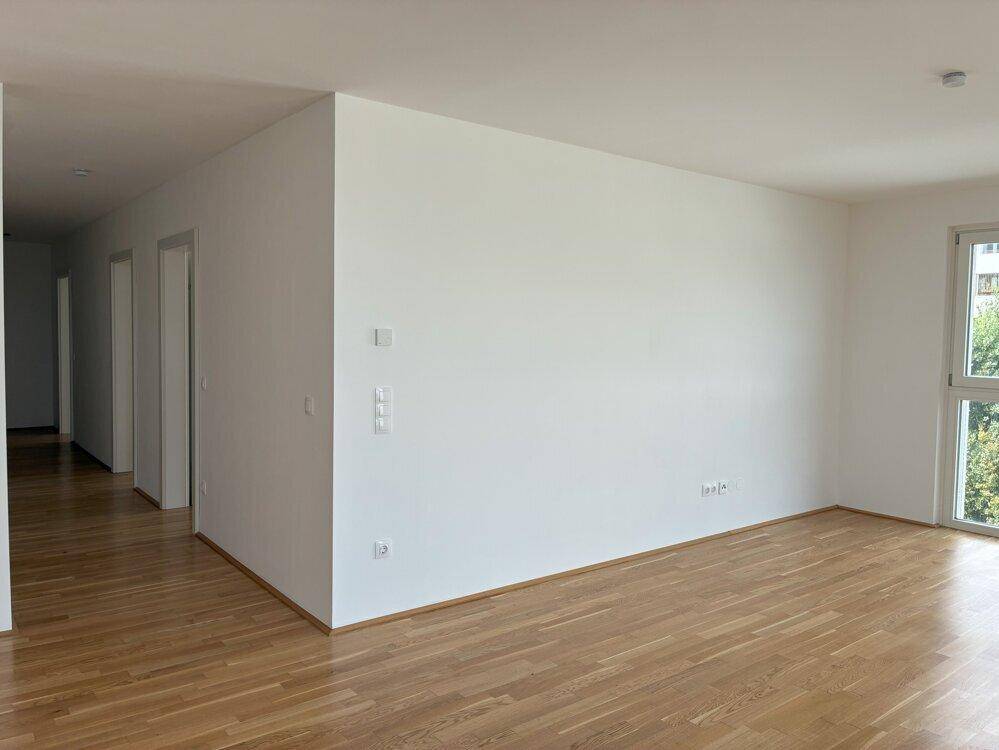 Heller, leerer Wohnbereich mit Holzboden und Zugang zu einem Flur.