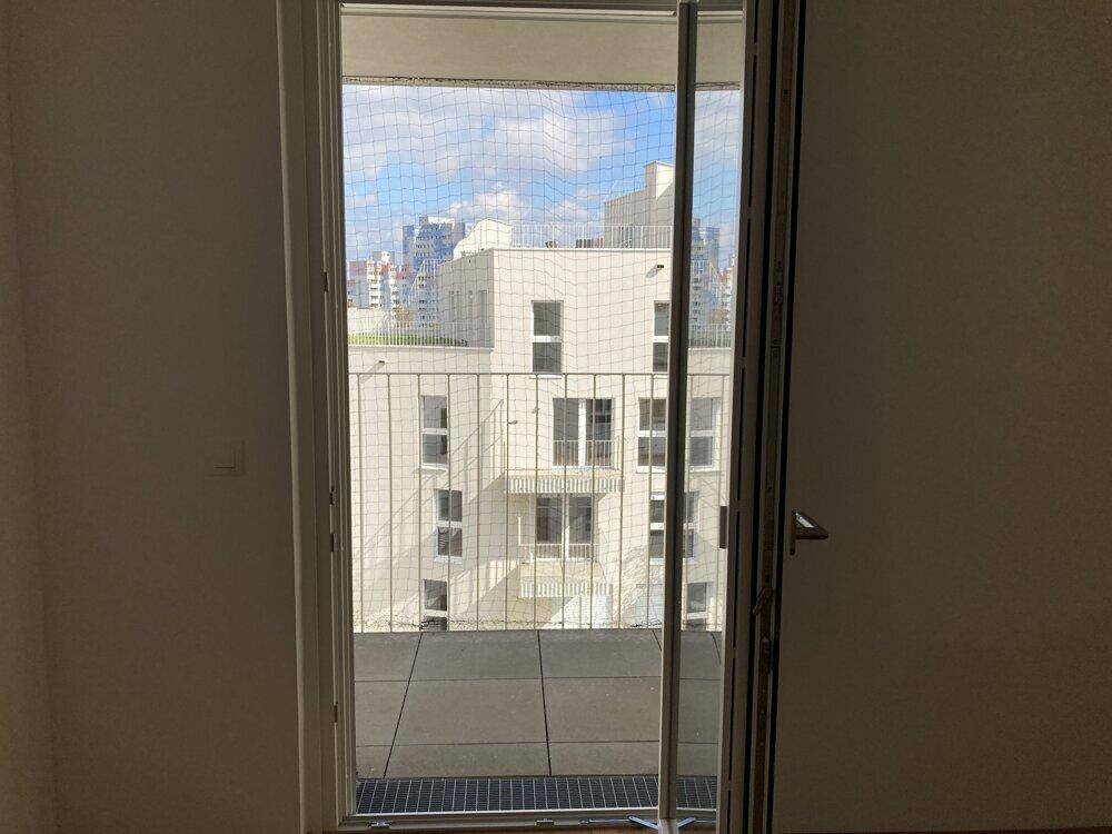 Blick aus einem Zimmer durch die Balkontür auf die umliegenden modernen Wohngebäude.