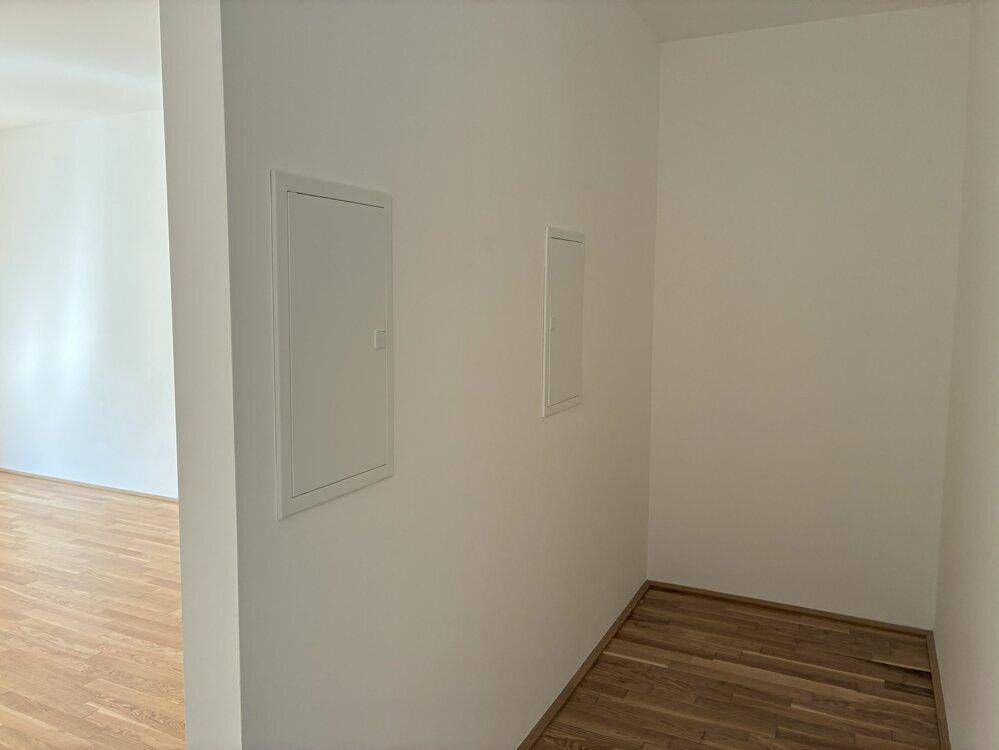 Kleiner Flurbereich mit Parkettboden und Zugangsklappen in der Wand, unmöbliert und funktional.