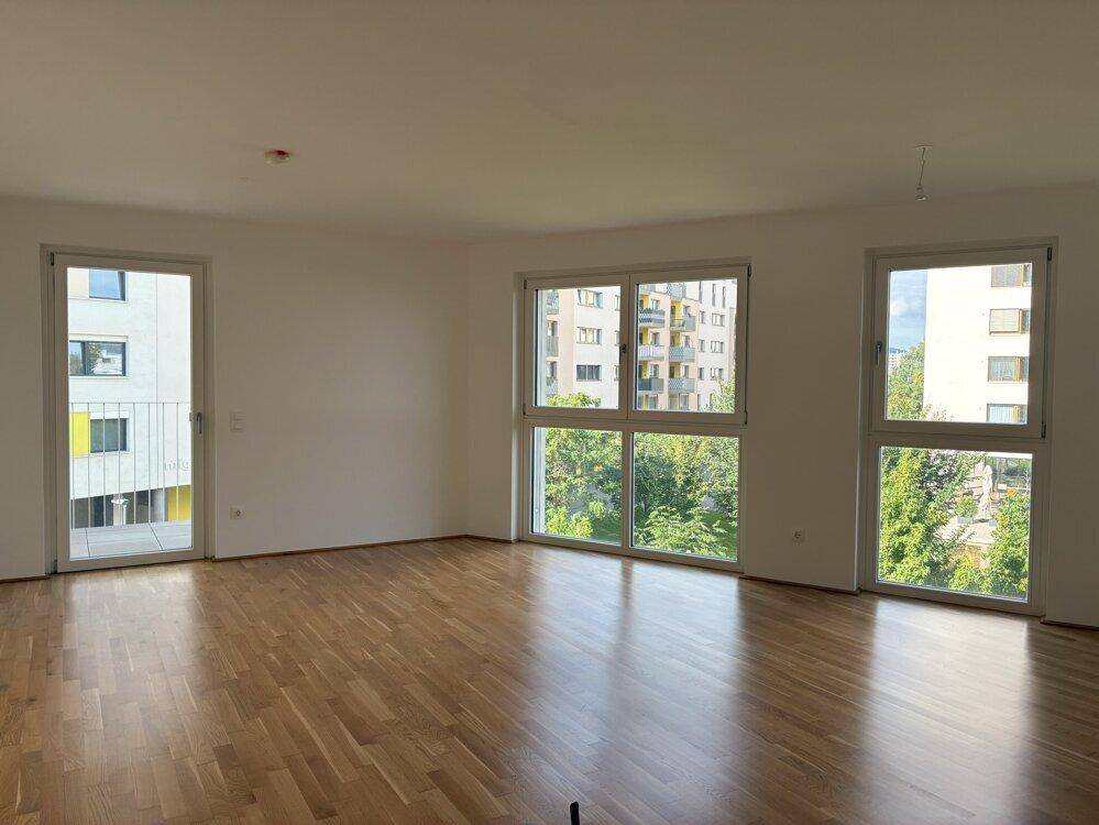 Geräumiges Wohnzimmer mit hellem Parkettboden, großen Fenstern und Blick ins Grüne.