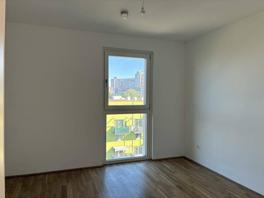 Helles Schlafzimmer mit Parkettboden und Blick auf die umliegenden Gebäude.