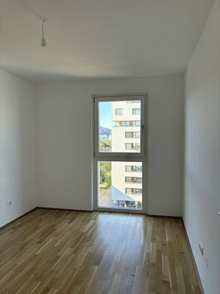Geräumiges Schlafzimmer mit hellem Parkettboden und großem Fenster, das viel Tageslicht hereinlässt.