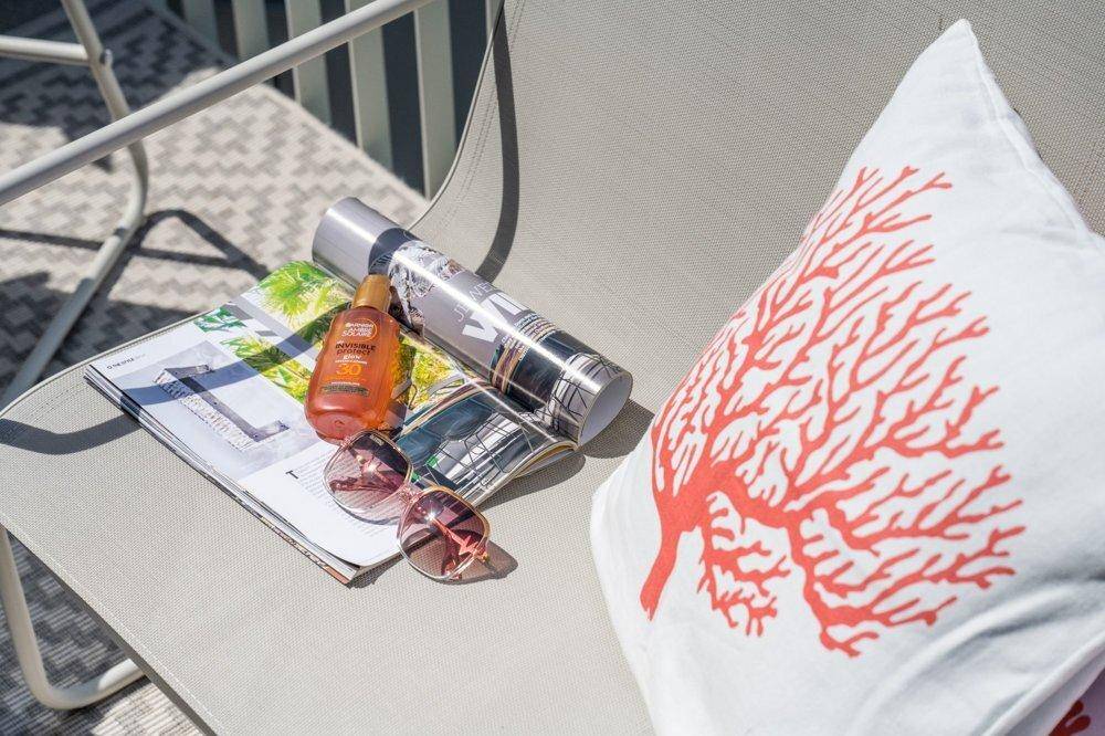 Nahaufnahme eines Balkonstuhls mit dekorativem Kissen, Sonnenbrille und Magazin für entspannte Stunden.
