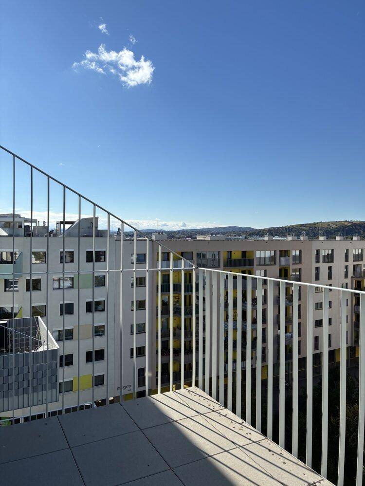 Heller Balkon mit Fliesenboden und weitem Blick über die umliegenden Gebäude und Hügel.
