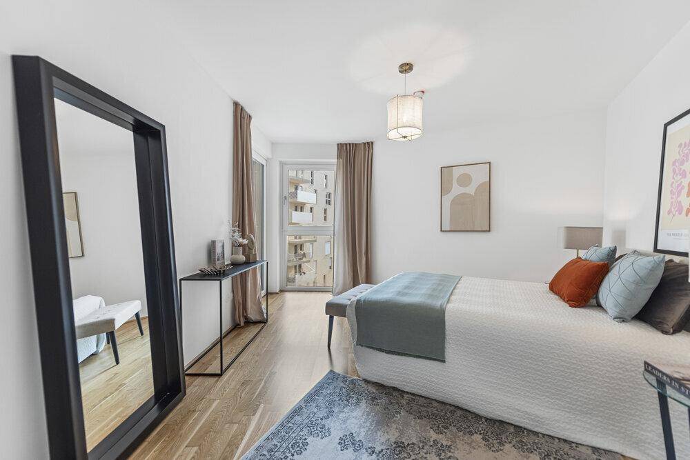 Helles Schlafzimmer mit Holzboden, großem Spiegel und Zugang zum Balkon.