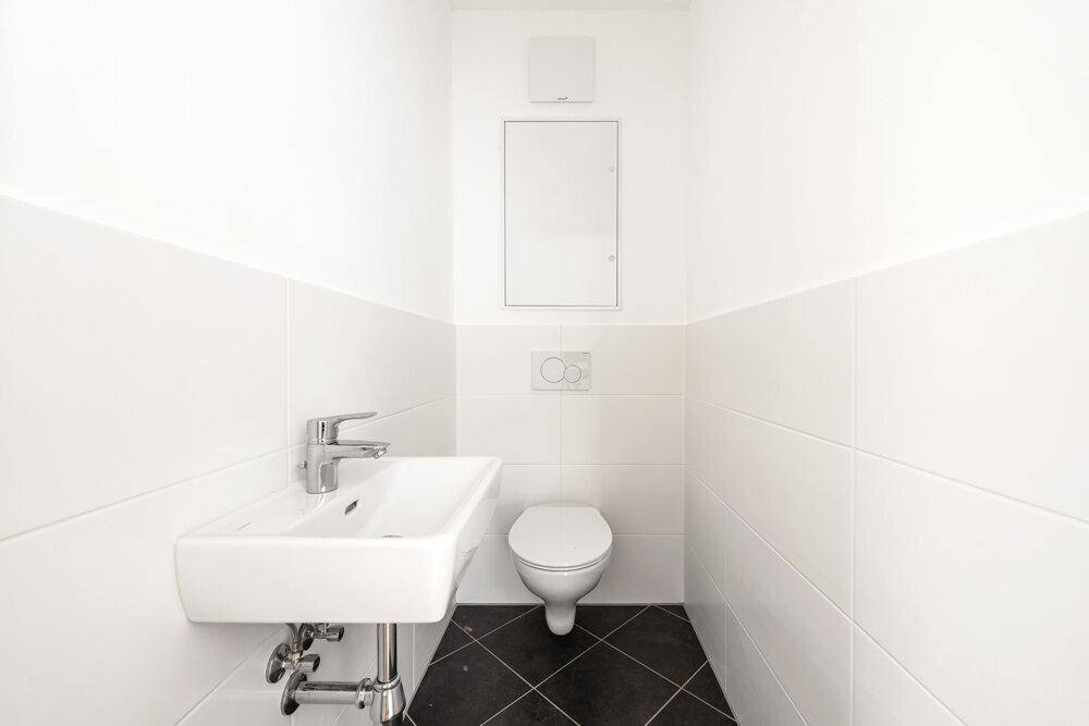 Modernes Gäste-WC mit weißen Fliesen, schwarzem Boden und wandhängendem WC.
