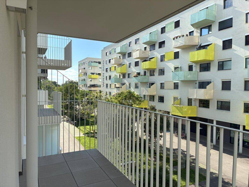 Balkon mit Fliesenboden und weitem Blick auf die moderne Wohnanlage mit farbigen Balkonen.