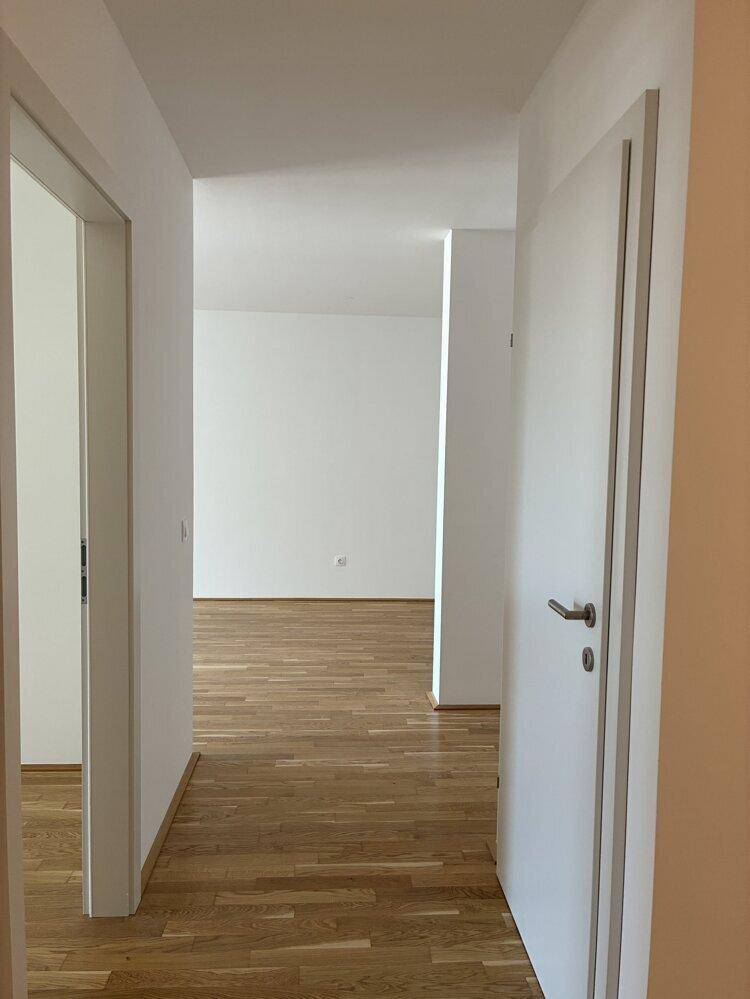 Blick aus einem Flur in einen hellen Raum mit Holzboden und weißen Wänden.