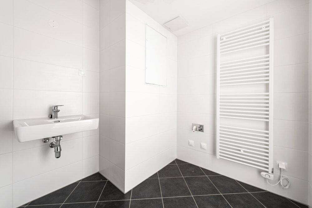 Helles Badezimmer mit Waschbecken, Handtuchheizkörper und dunklen Bodenfliesen.