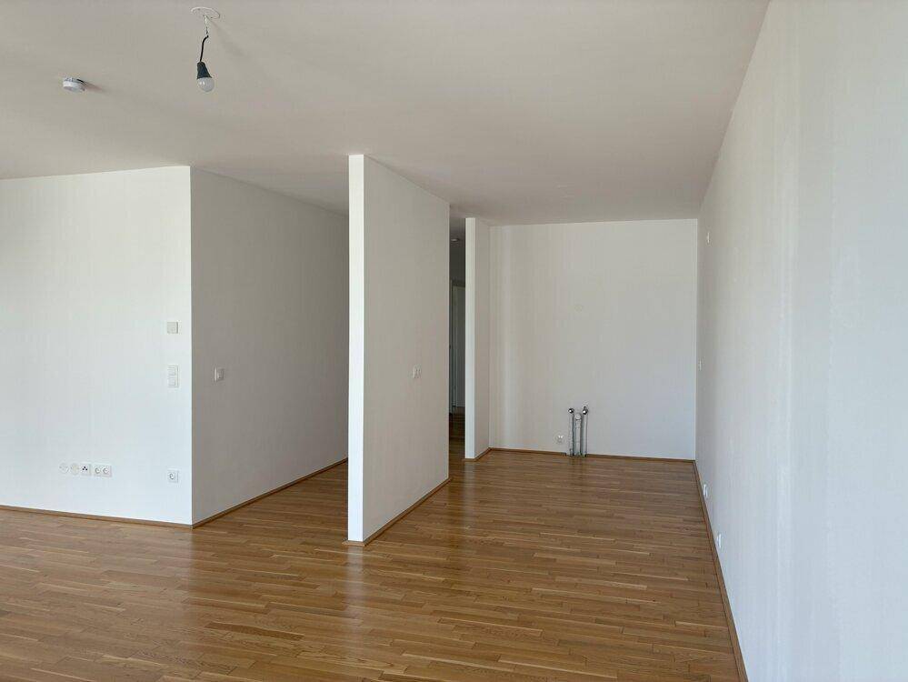 Großer, heller Raum mit Holzboden und vorbereiteten Anschlüssen für eine Küche oder Bad.