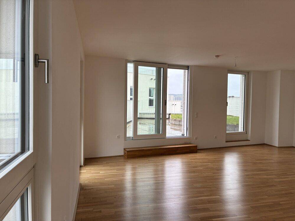Helles Wohnzimmer mit Parkettboden und großen Fenstern, die viel Tageslicht hereinlassen.