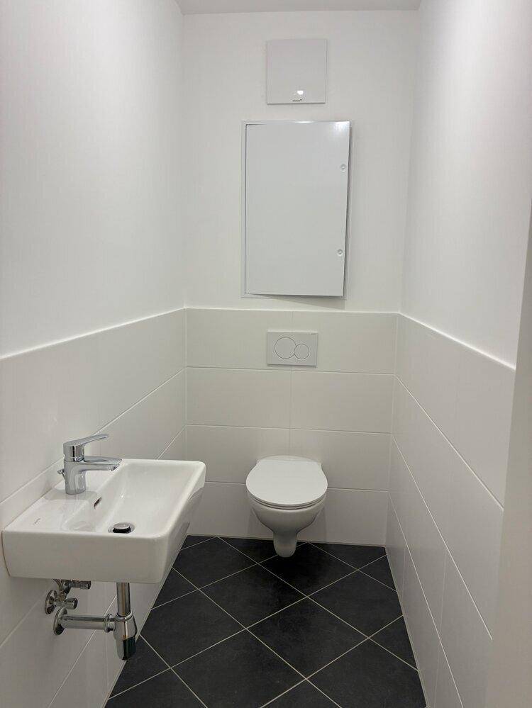 Funktionales Gäste-WC mit wandhängender Toilette, kleinem Waschbecken und modernen Fliesen.