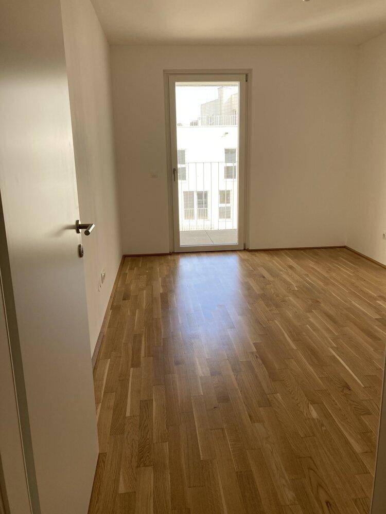 Helles Zimmer mit Parkettboden und Zugang zu einem Balkon, ideal als Schlaf- oder Arbeitszimmer nutzbar.