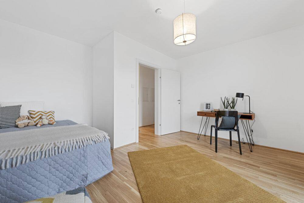 Helles Schlafzimmer mit Holzboden, Schreibtisch und einfacher, moderner Einrichtung.