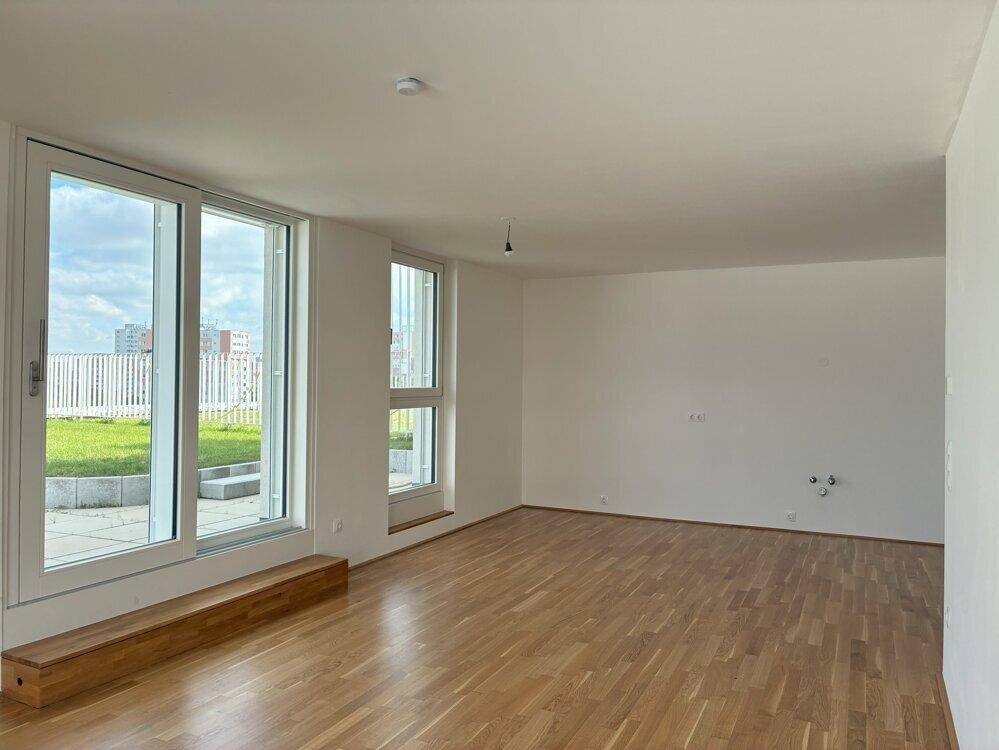 Heller Raum mit Holzboden und großen Fenstern, vorbereitet für eine moderne Küche.