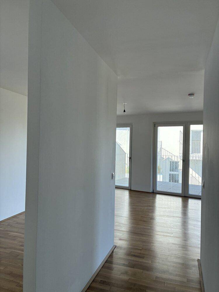 Heller Flur mit Parkettboden, der in einen Wohnbereich mit Balkonzugang mündet.