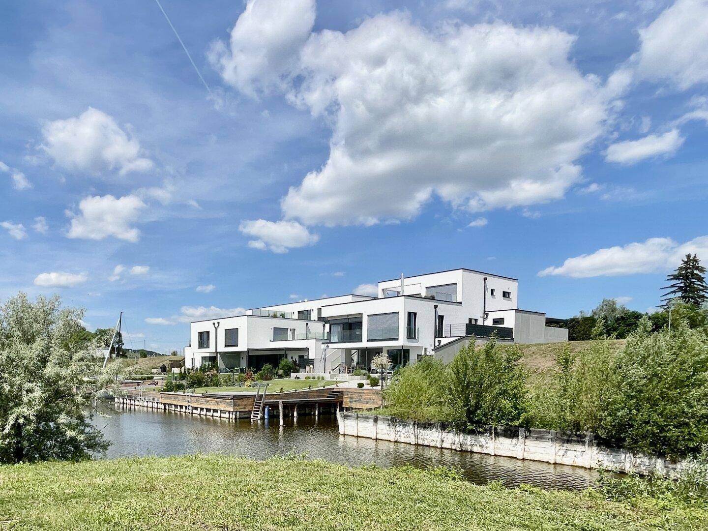 Reihe moderner Häuser mit großen Fensterfronten und Terrassen direkt am Wasser gelegen.