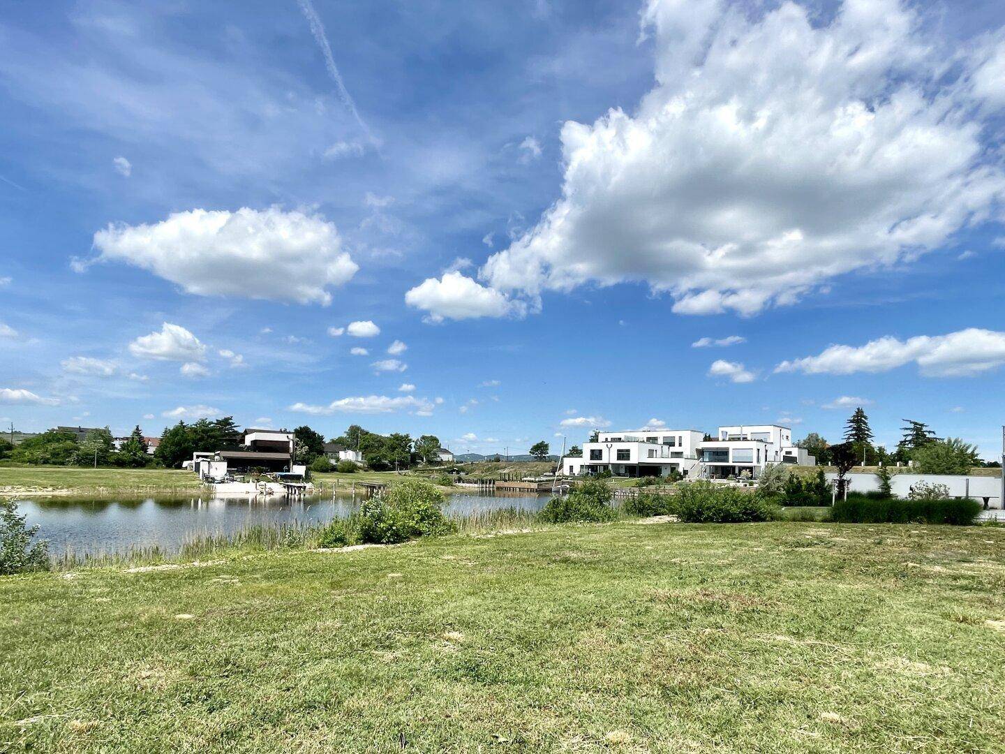 Panoramablick auf moderne Häuser am Seeufer, umgeben von grüner Landschaft.