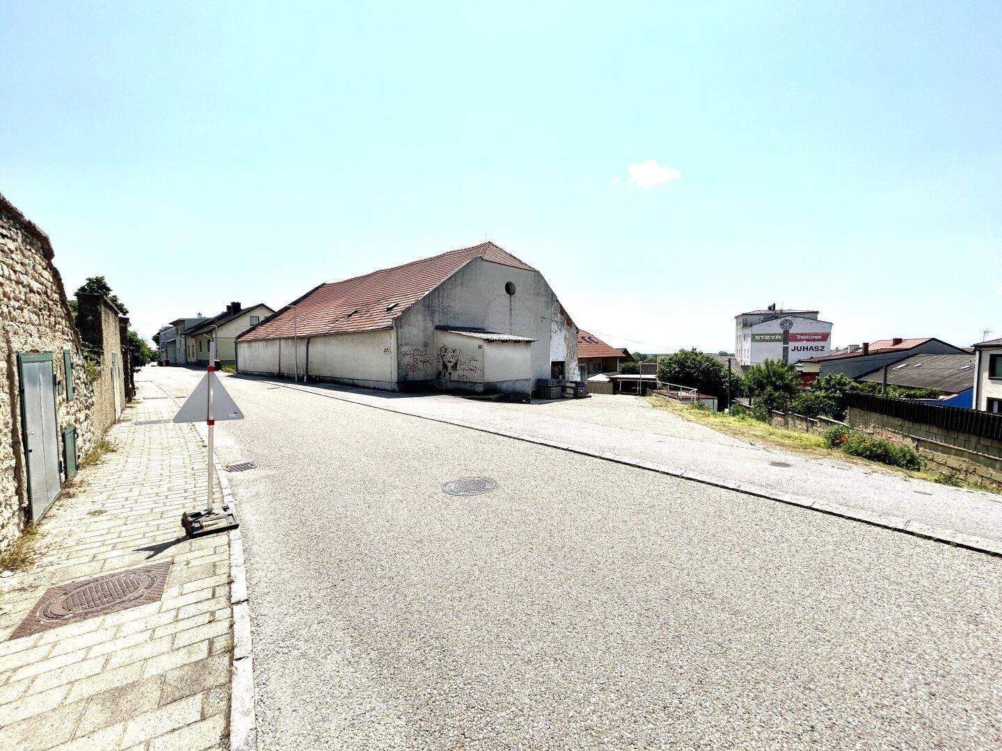 Längliche Ansicht des alten Gebäudes mit Ziegeldach und angrenzender Straße.