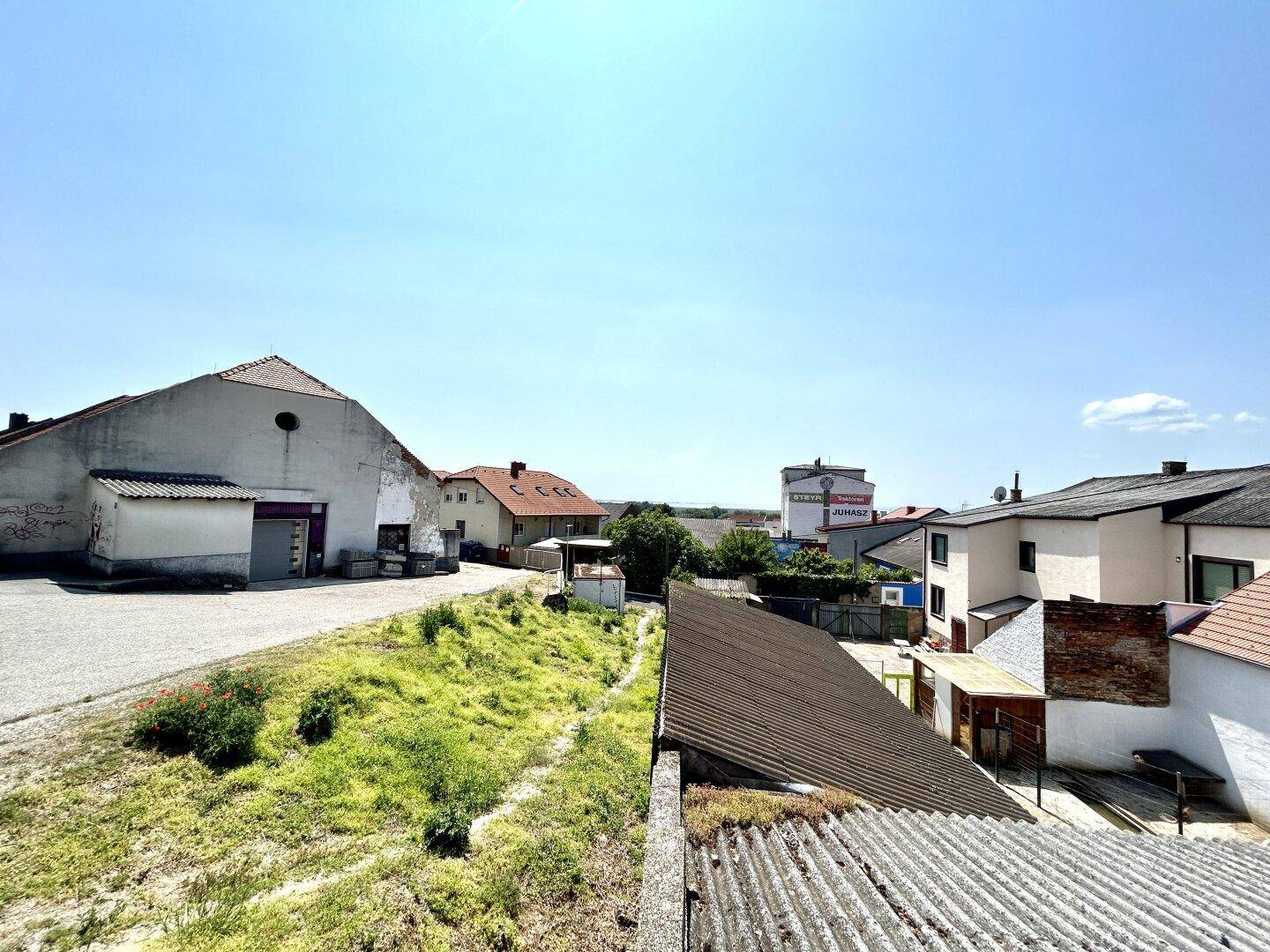 Blick über ein Wellblechdach auf das alte Gebäude und die umliegende Bebauung.