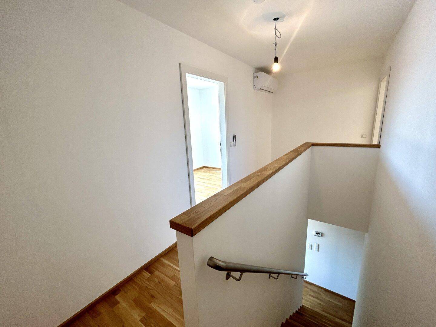 Heller Flur mit Holzgeländer und Treppe, ausgestattet mit einer Klimaanlage.