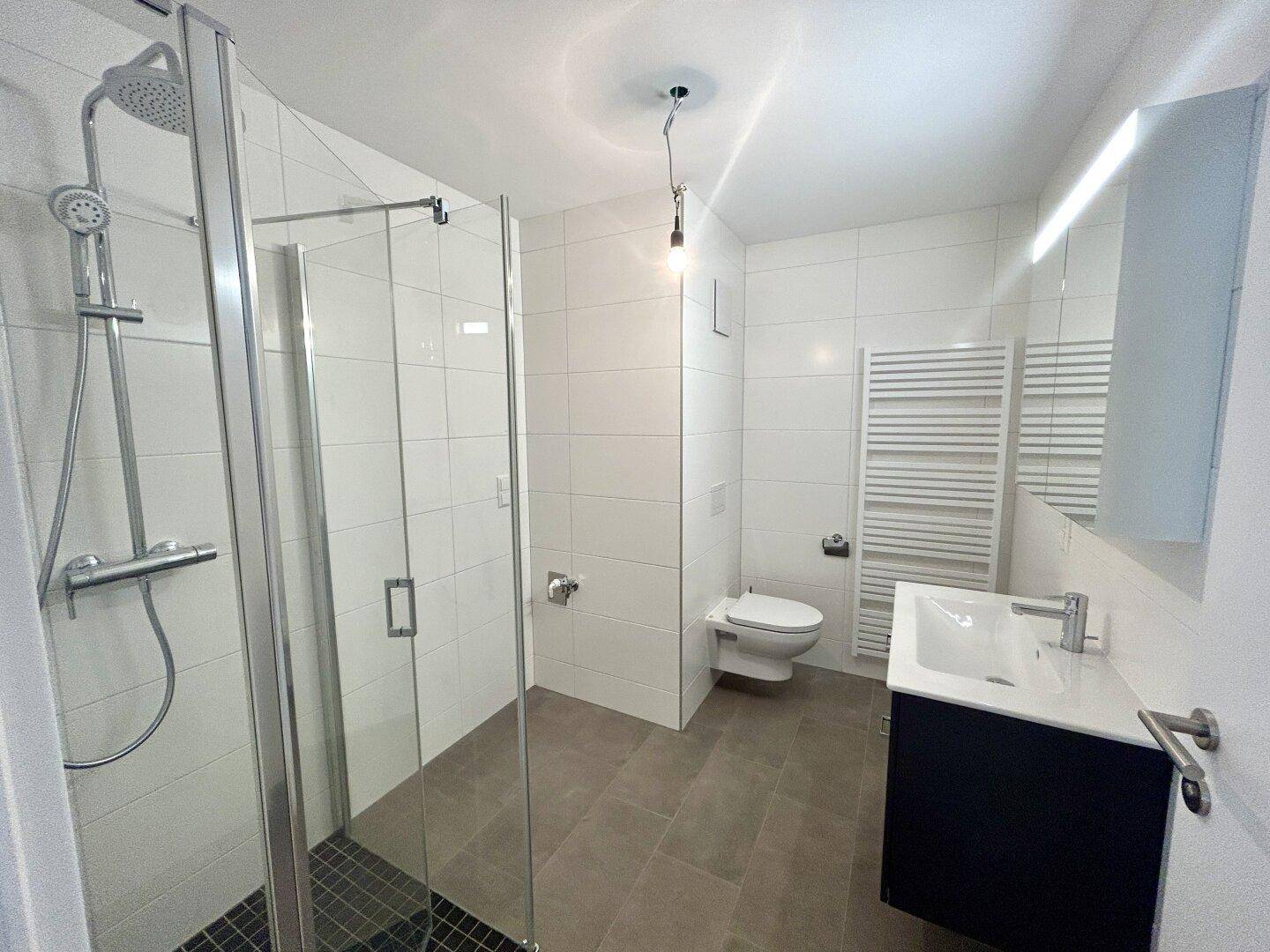 Zeitgemäßes Badezimmer mit Dusche, wandhängendem WC und beheiztem Handtuchhalter.