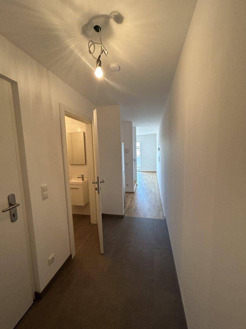 Heller Flur mit Fliesenboden, der zu weiteren Räumen mit Parkett führt.