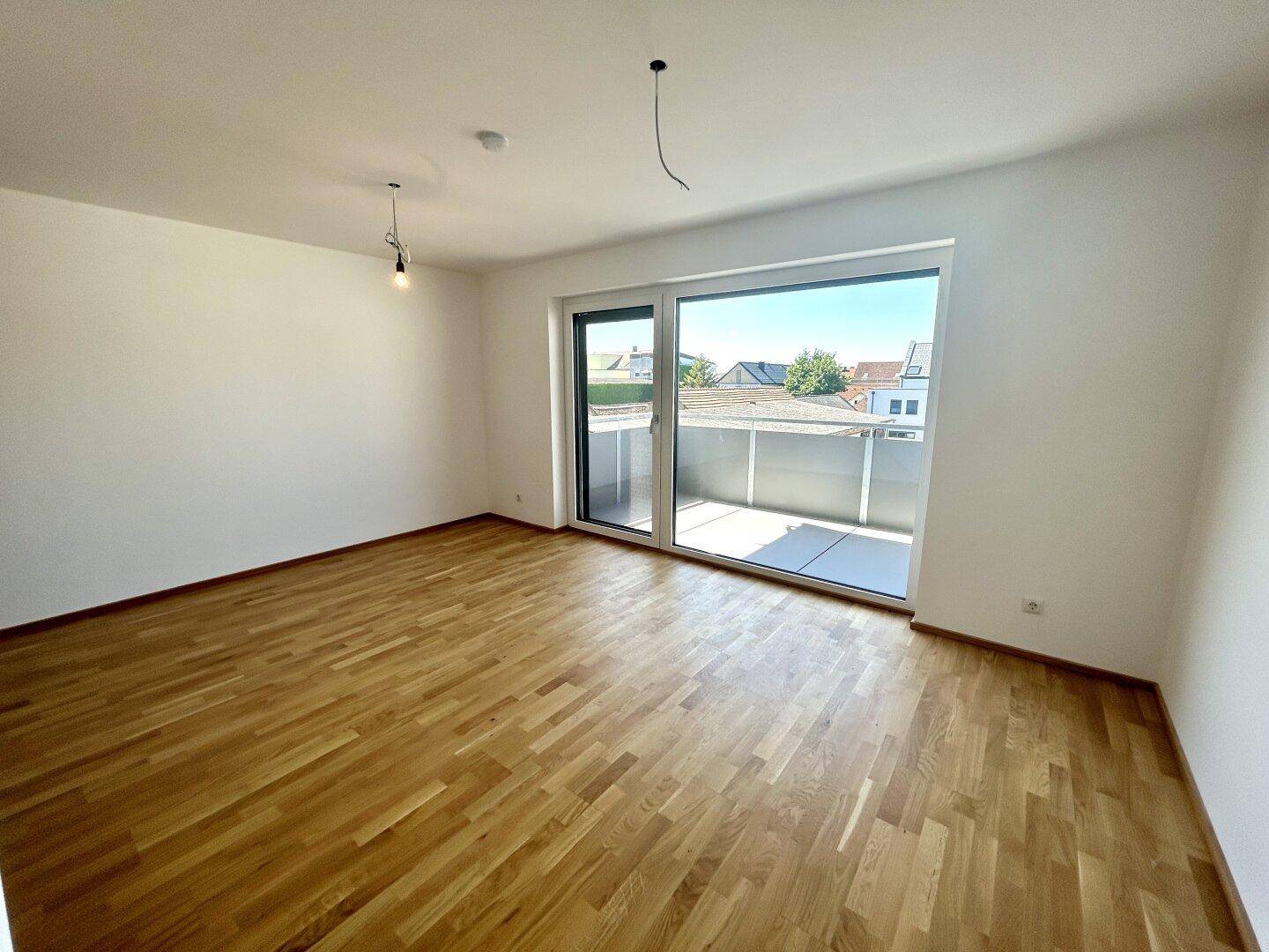 Geräumiger Raum mit Parkettboden und großer Glasfront, die auf einen Balkon führt.