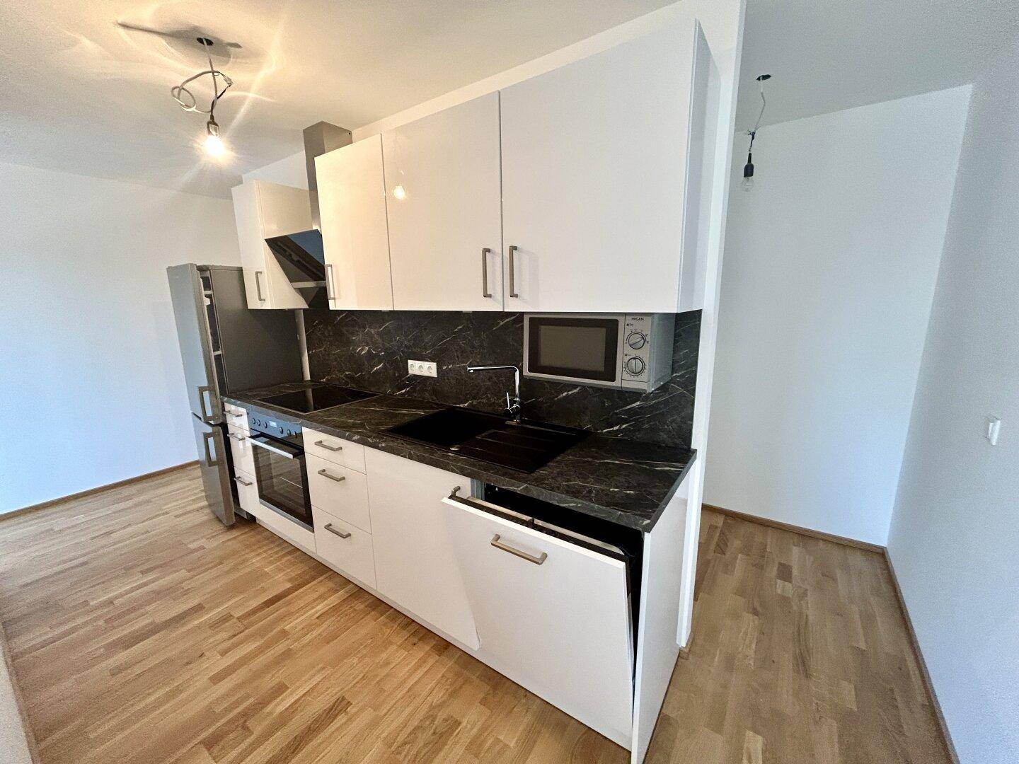 Moderne Einbauküche mit weißen Hochglanzschränken, dunkler Arbeitsplatte und integrierten Geräten.