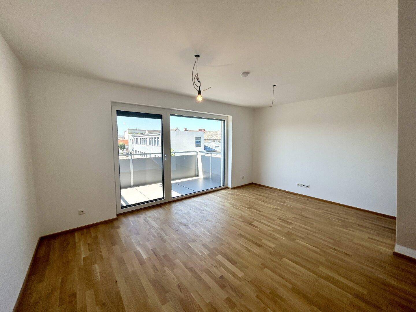 Heller Wohnraum mit Parkettboden und Zugang zu einem sonnigen Balkon.
