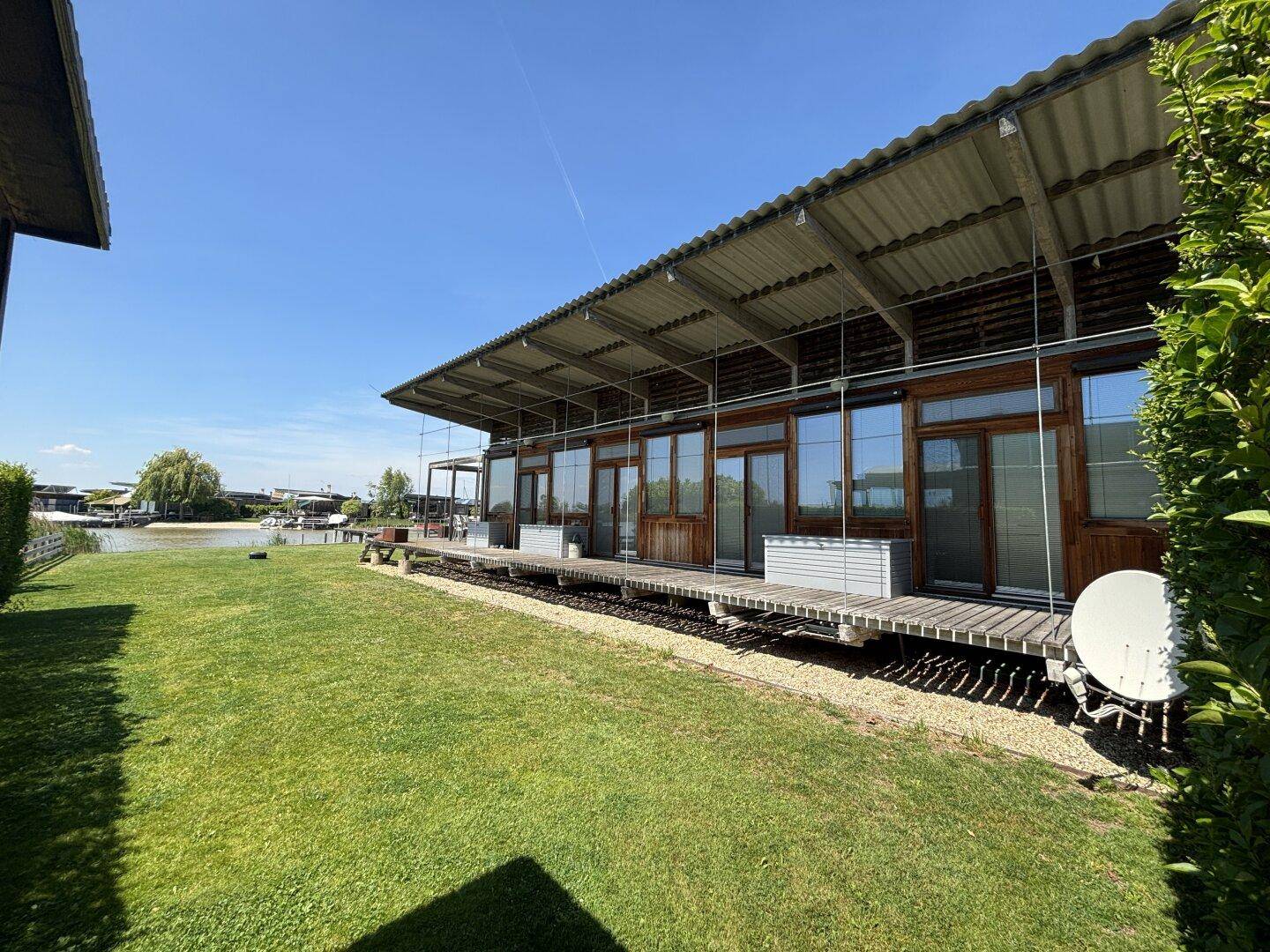 Moderne Architektur mit weitläufiger Holzterrasse und gepflegtem Rasen am Seeufer.