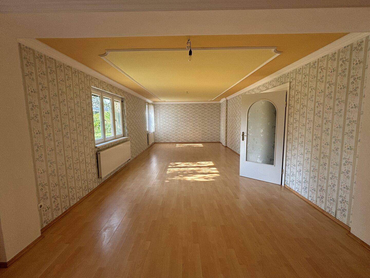 Heller Wohnraum mit Parkettboden, gemusterter Tapete und dekorativer Deckenverzierung.