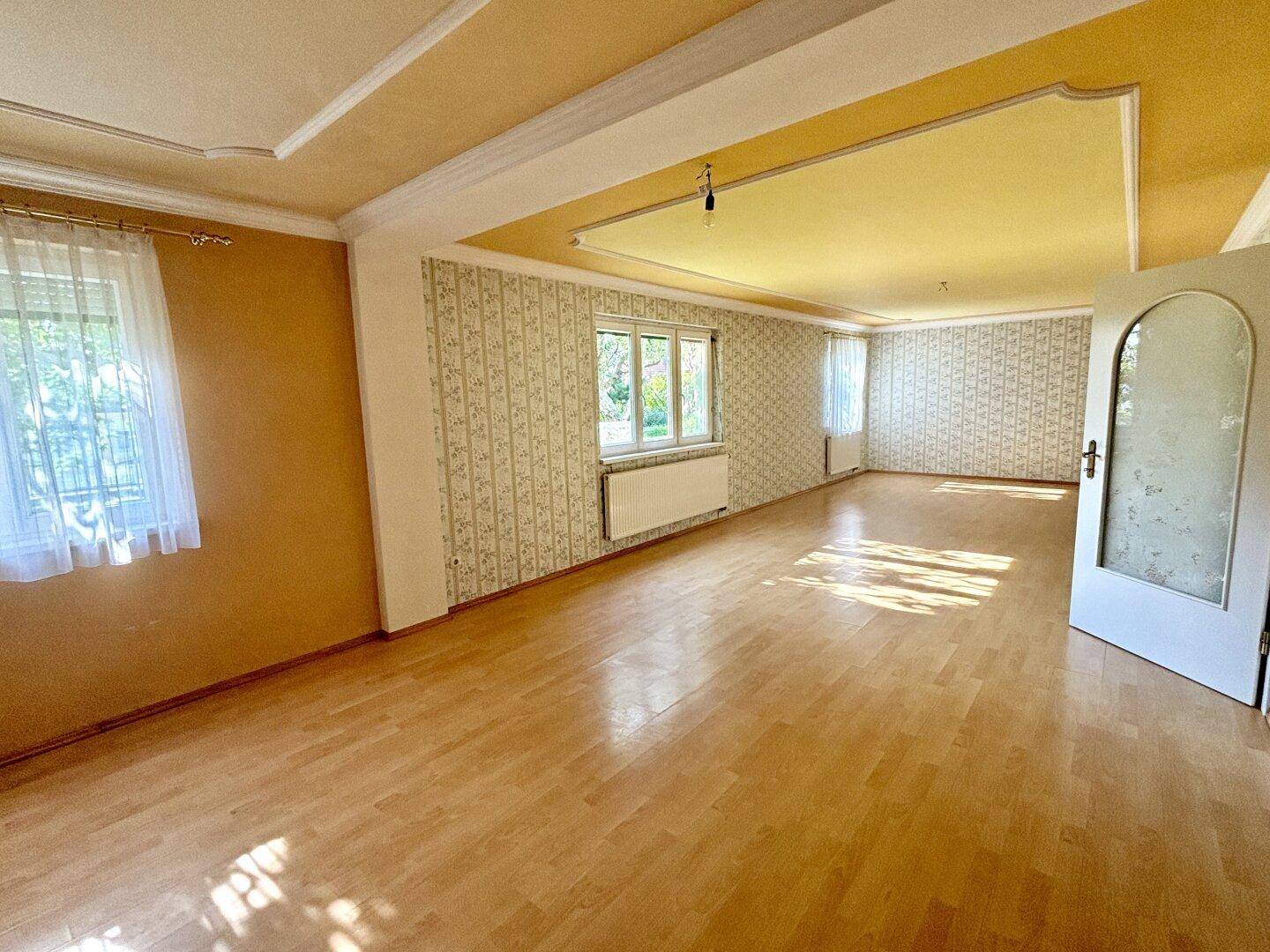 Langer Wohnraum mit Parkettboden, gemusterter Tapete und Fenstern für viel Tageslicht.