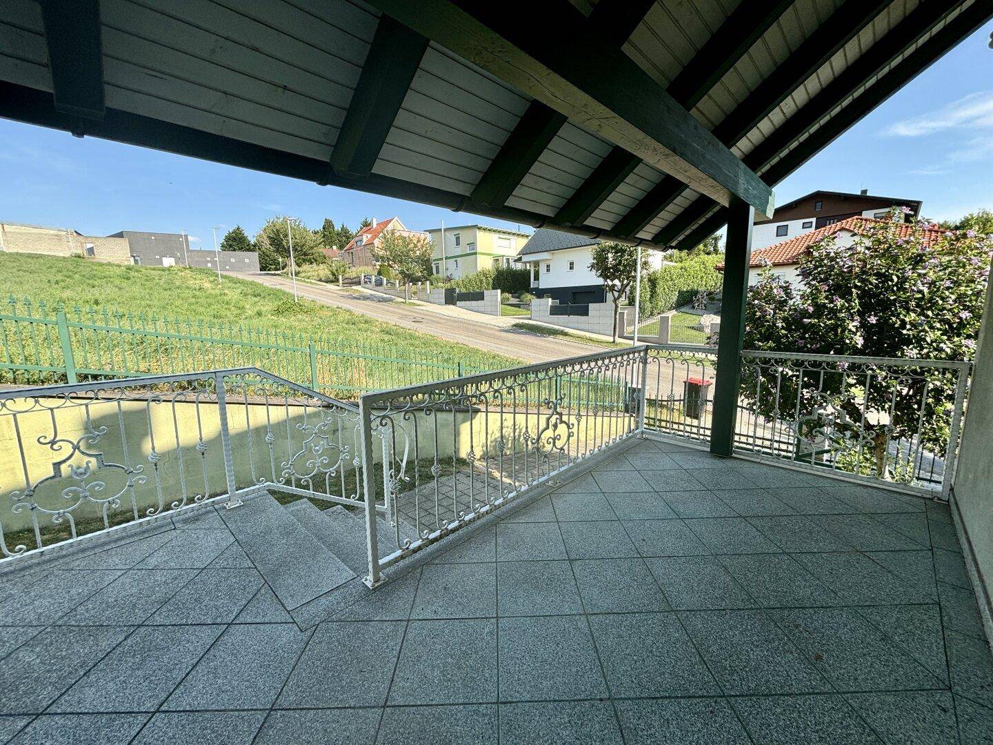 Überdachter Balkon mit Fliesenboden und schmiedeeisernem Geländer, Blick auf die Straße.