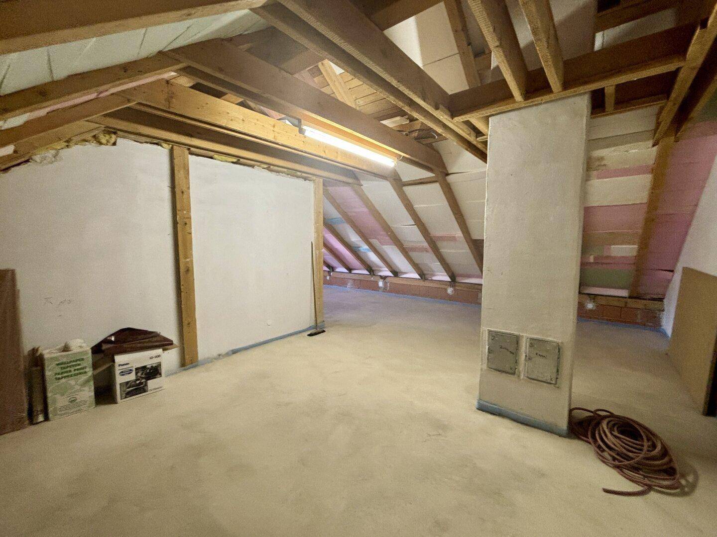 Ausbaufähiger Dachboden mit sichtbaren Holzbalken und unfertigen Wänden.