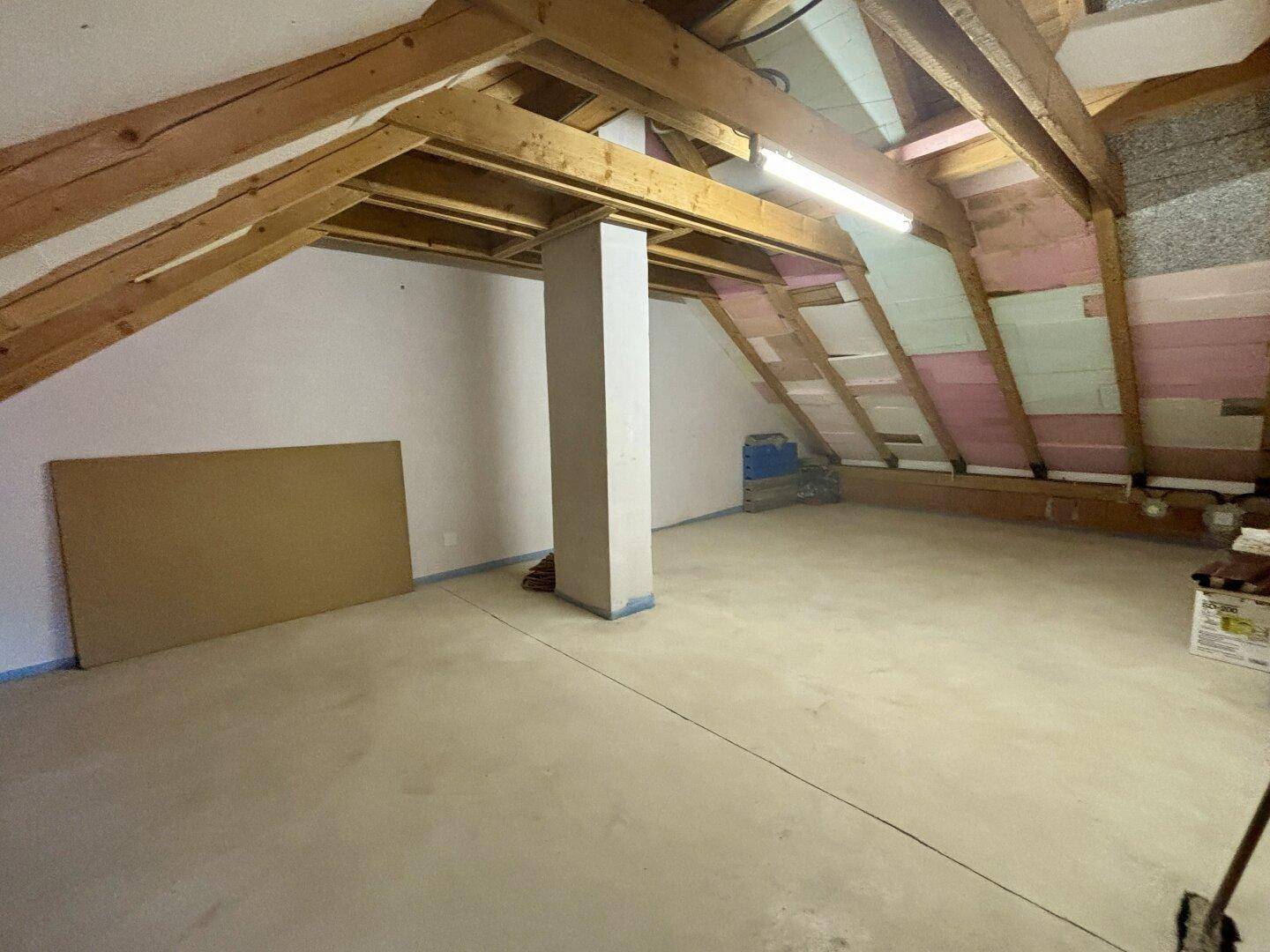 Geräumiger Dachboden mit sichtbaren Holzbalken und unfertigen Wänden, ideal für Ausbau.