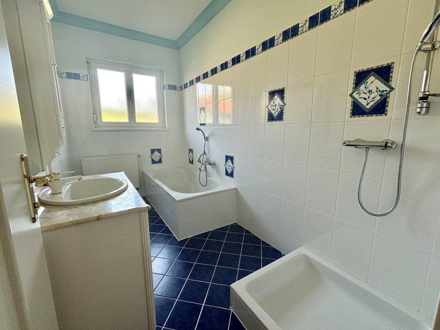 Badezimmer mit blauen und weißen Fliesen, Badewanne, Dusche und Fenster.