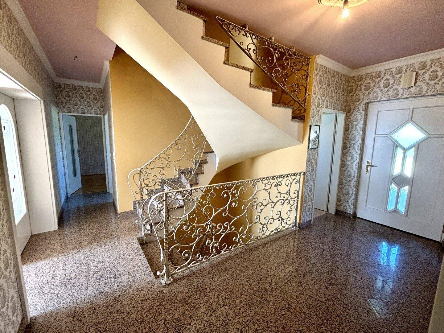 Eingangsbereich mit Terrazzoboden, geschwungener Treppe und dekorativem Geländer.