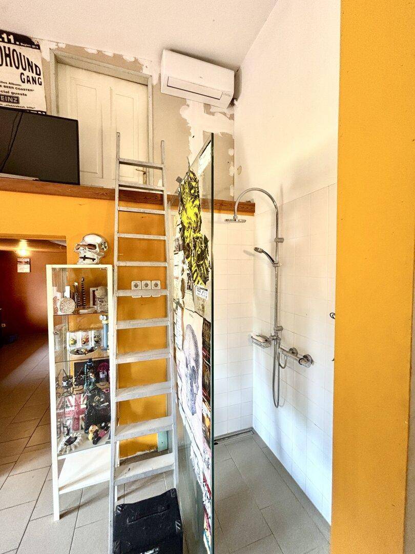 Offener Wohnbereich mit Duschbereich und einer Leiter, die zu einem Hochbett oder Stauraum führt.