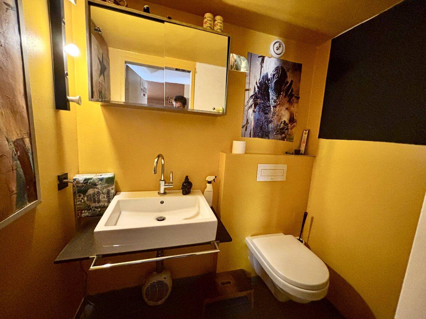 Modernes Gäste-WC mit gelben Wänden, wandmontierter Toilette und einem stilvollen Waschbecken.